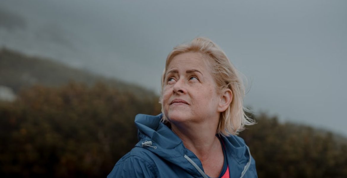 Portrait of a senior woman outdoors in a blue jacket, looking upwards with a thoughtful expression.