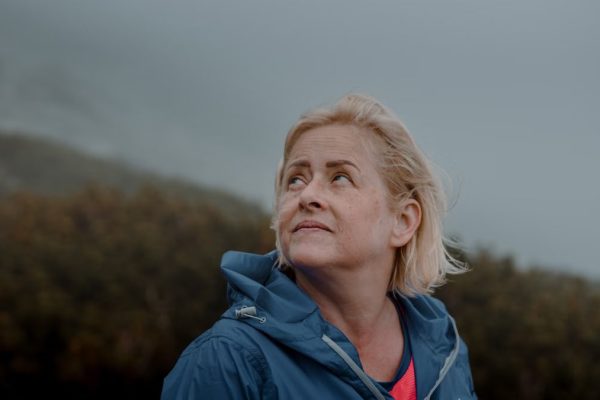 Portrait of a senior woman outdoors in a blue jacket, looking upwards with a thoughtful expression.